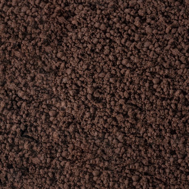 Nahaufnahme einer dunkelbraunen, krümeligen Oberfläche, die grobem Erdreich oder Kaffeesatz ähnelt.