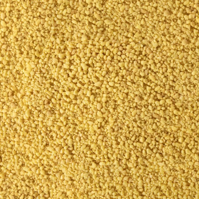 Nahaufnahme feiner gelber körniger Textur, ähnlich grobem Maisgrieß oder trockenem Couscous.