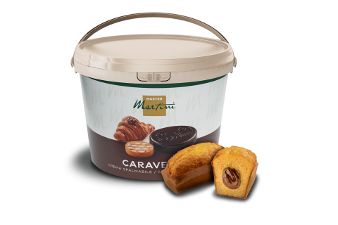 Ein großer Eimer Streichcreme Master Martini Caravella neben einem Mini-Kuchen mit Schokoladencreme-Füllung.