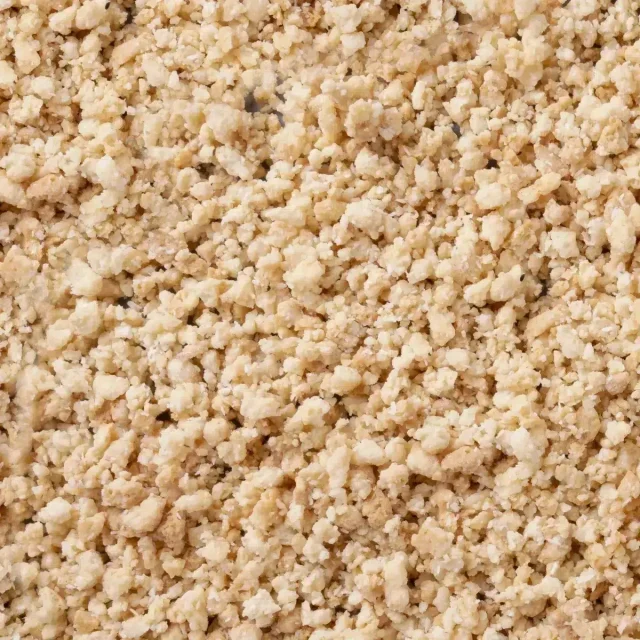 Nahaufnahme heller, krümeliger Granulate mit grober, bröseliger Textur über das gesamte Bild.